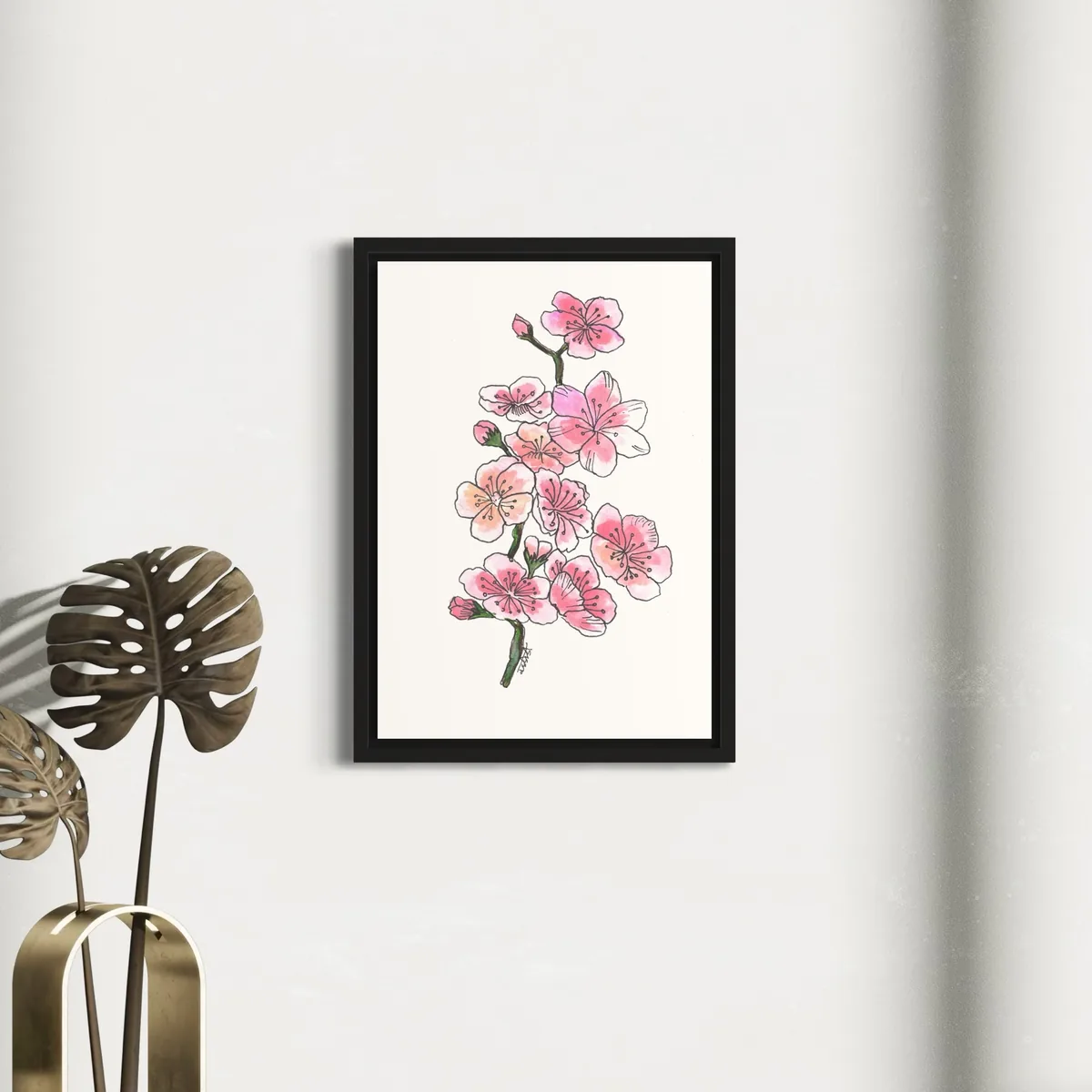 Watercolor floral sketch of pink blossoms in a black frame on a white wall.