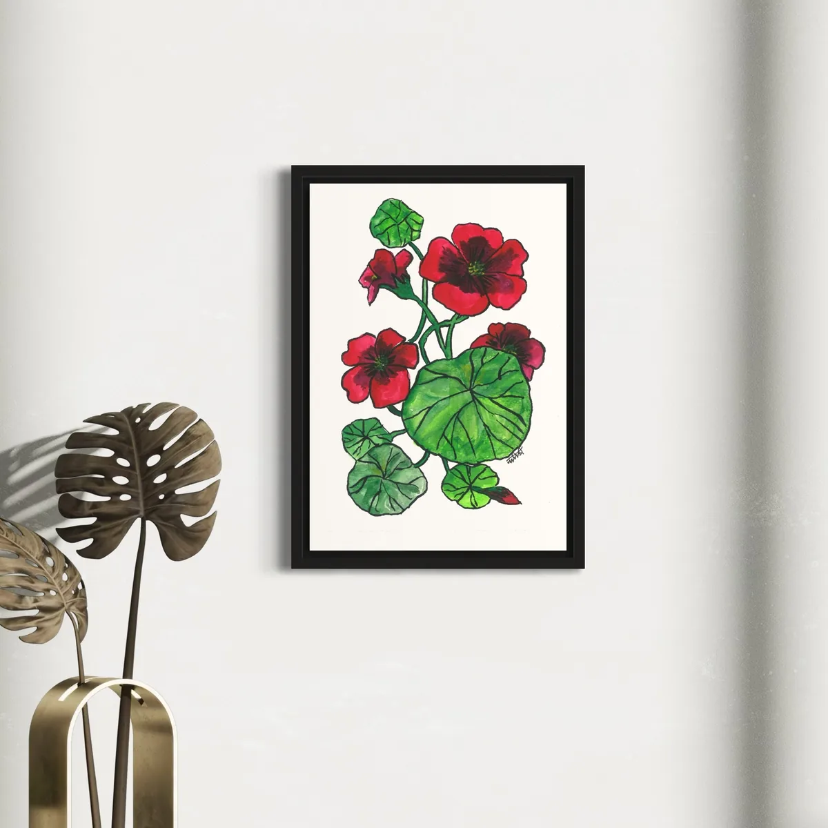 Vibrant red and green watercolor flowers in a black frame against a white wall.