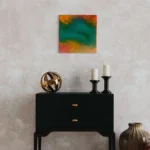 Abstract acrylic artwork featuring vibrant emerald, teal, and orange fluid colors on a light wall.