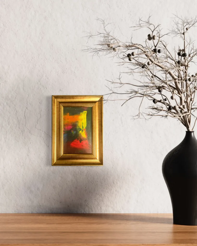 Gold framed abstract artwork featuring vibrant yellows, reds, and oranges on a light wall.